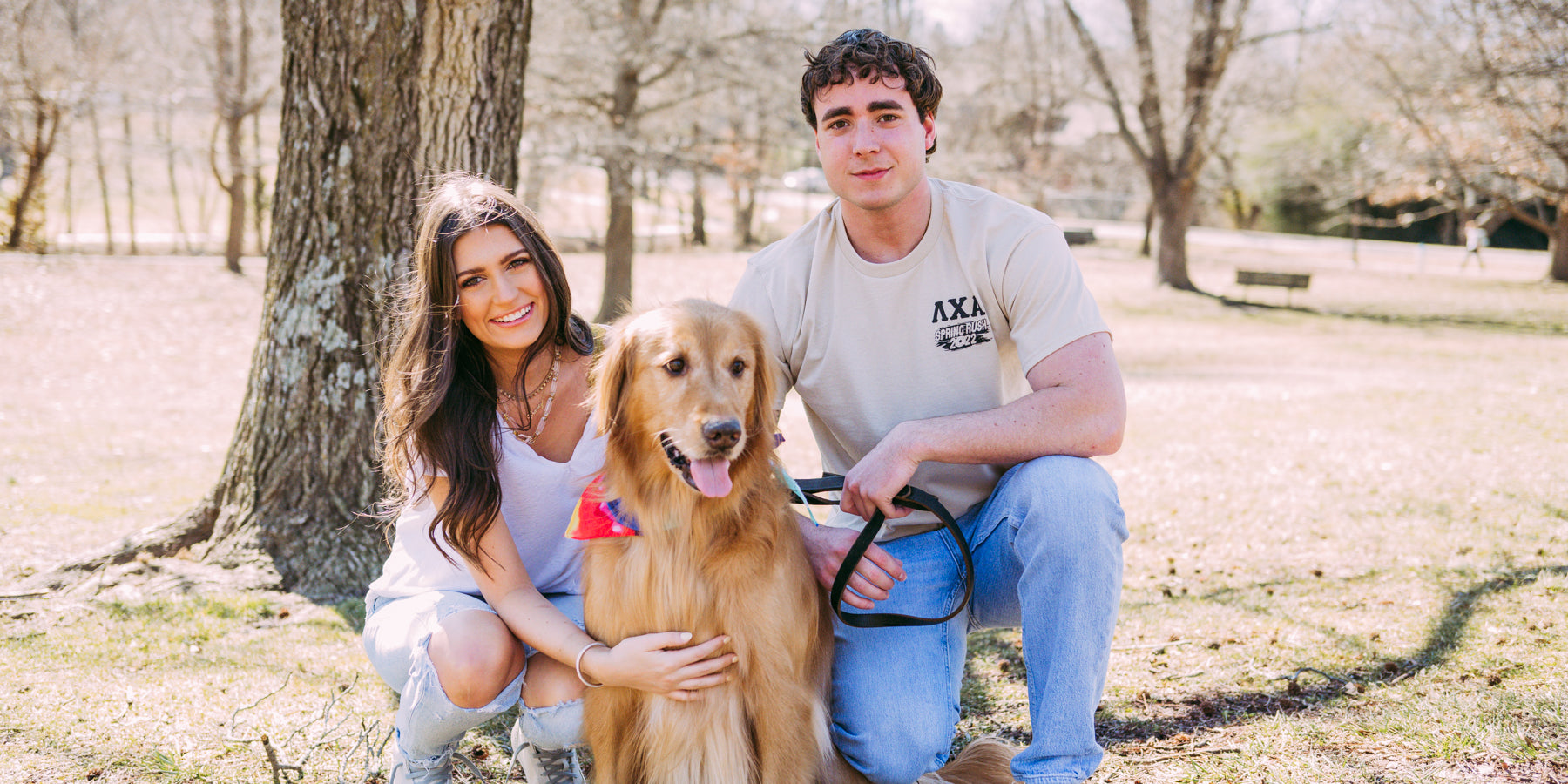 Girl, boy, and dog stand in the park facing the camera. Boy wears a cream Lambda Chi Shirt with the LXA letters on the left.